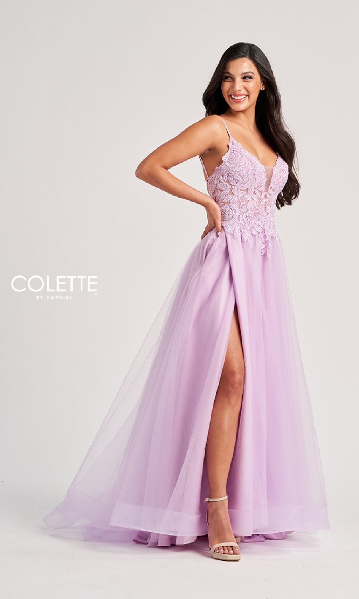 A woman wearing the Colette CL8100 Long Prom Dress, featuring a sleeveless pastel design with lace embroidery on the bodice and a high slit, smiles as she poses against a plain background.
